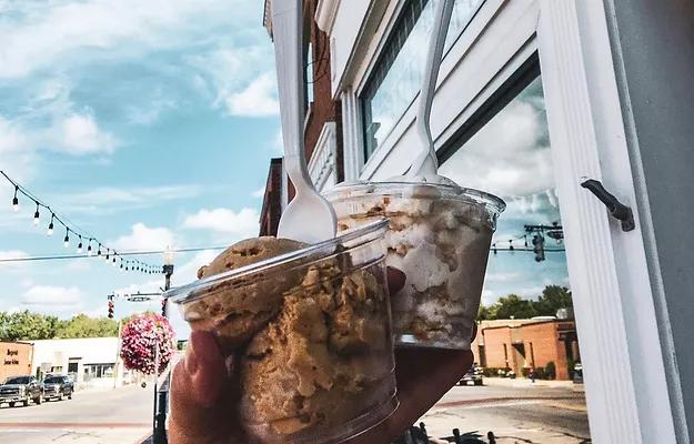 A hand can be seen holding 2 types of ice creams in a cup in front of The Coffee Hall and Creamery in Marysville Ohio.