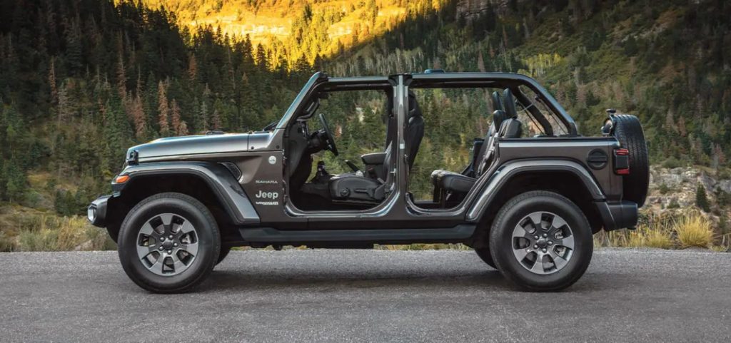 A side profile of the 2022 Jeep Wrangler with 4 doors but the doors are taken off. The Jeep is empty and on a mountain road.