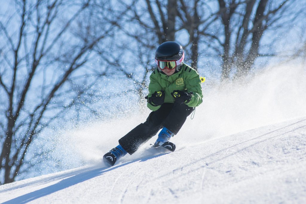 A boy in a green jacket is skiing down a hill.