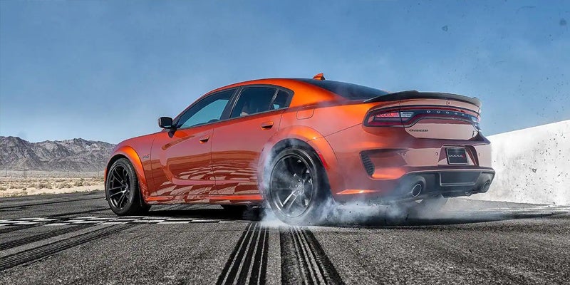 An orange 2023 Dodge Charger making a turn and burning rubber.