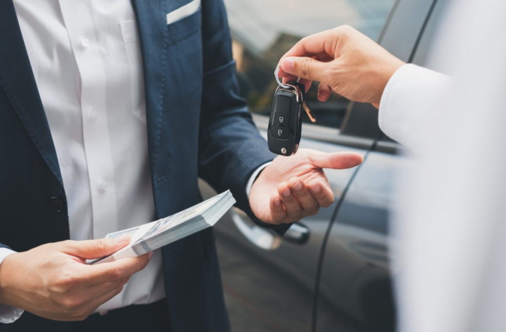 A vehicle salesman exchanging money and key for a car to a new owner.